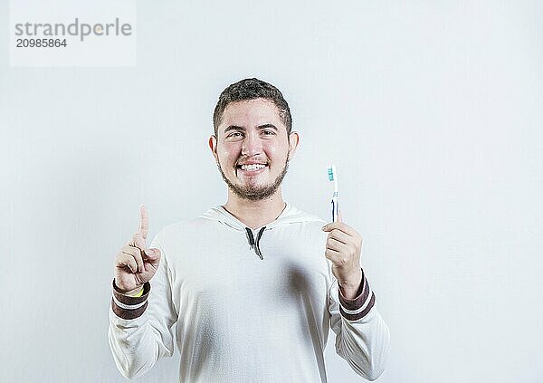 Positive young man holding toothbrush pointing up. Happy guy holding toothbrush and pointing up