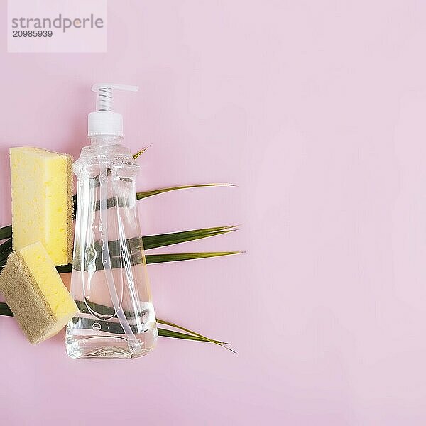 Flat lay with green palm leaf  soap dropper  dishwashing liquid  dish soap  washcloth on pastel pink and yellow background.