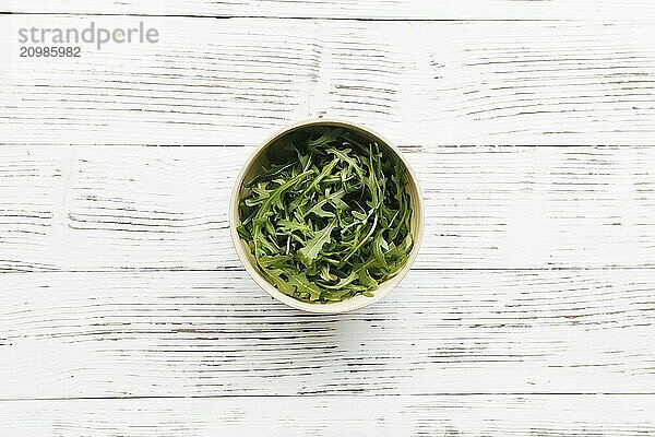 Green fresh arugula salad leaves in bowl on white wooden background. Healthy eating concept.