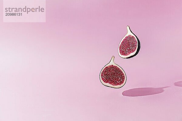 Fresh tasty fig fruit halves levitation with shadow on pink background. Two cross sections of fig falling down or fly. Vegan desert concept. Shadow of flying healthy eating food.