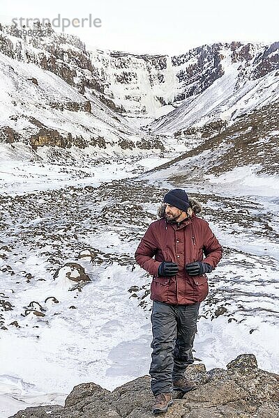 Portrait of a hiker at frozen Hengifoss waterfall in cold Iceland winter  volcanic cliffs