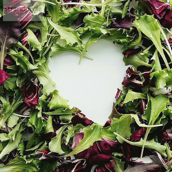 Heart shape from green and purple salad leafs mix background. White table.