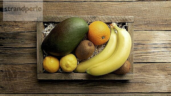 Fresh tropical fruits in a wooden delivery box on a wooden background. Orange  banana  mango  kiwi and lemon top view flat lay with copy space for some advertisement text