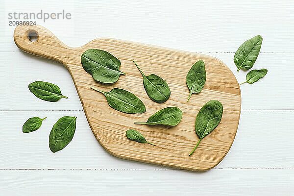 Wooden cutting board with fresh green salad leaves of spinach on white background. Healthy vegetarian eating concept.