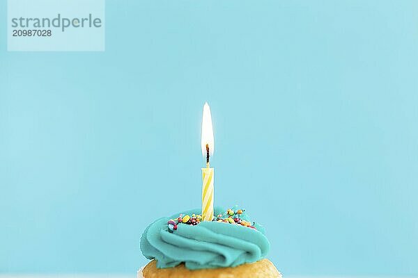 Birthday greetings concept. Burning candle on a muffin or cupcake. Blue background