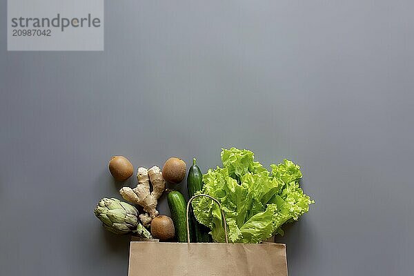 Healthy and organic food flay lay concept on gray background. Reusable eco bag with lettuce salad leaves  kiwi  cucumber  artichoke and ginger root