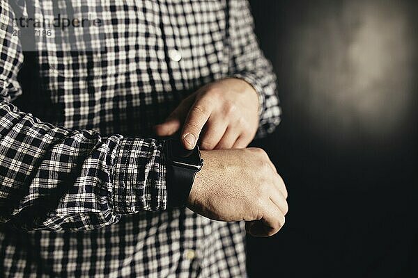 Man in casual clothes clicks hand watches  bracelet  black blurred background.