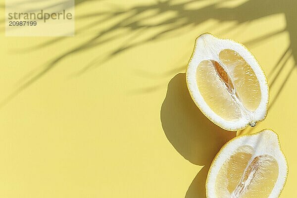 Two halved cuts of lemon with shadow from palm leaf on yellow background. Healthy eating  travel or vacation concept