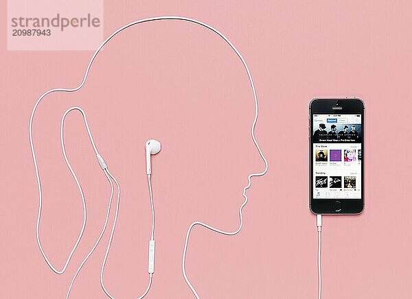 Woman head outline made by a headphones cord plugged into iPhone 5s smartphone with iTunes music store on its display. Creative concept on pink background