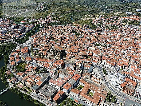 Aerial view of a town with red tiled roofs  river  bridge and green trees under a blue sky  aerial view  Plasencia  Jerte River  Cáceres  Caceres  Extremadura  Spain  Europe