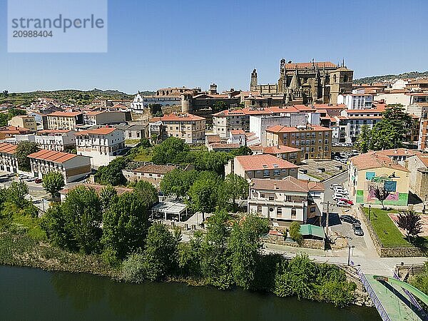 View of a town with a river in the foreground  traditional buildings and a church with red roofs  surrounded by trees and hills in sunny weather  aerial view  Plasencia  Jerte River  Cáceres  Caceres  Extremadura  Spain  Europe