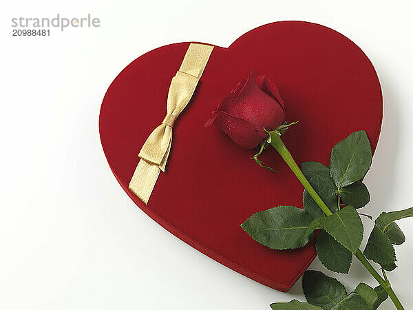 Red heart-shaped gift box and a red rose isolated on white background