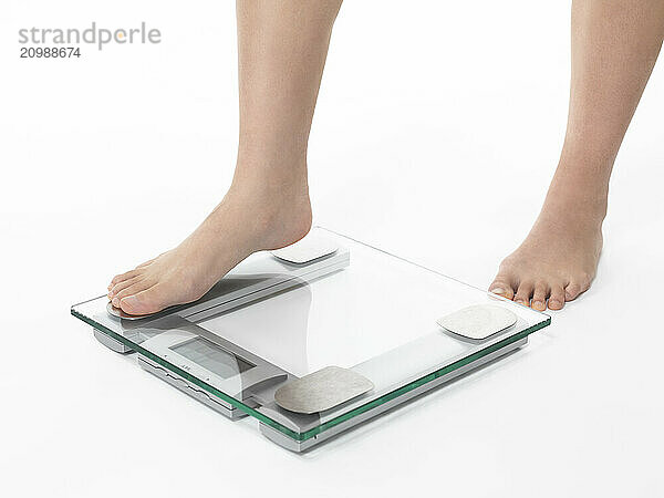 Closeup of woman legs stepping on weight scale. Isolated on white background