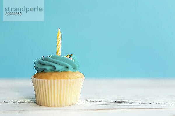 Birthday greetings concept. Yellow candle on a muffin or cupcake. Blue background. Wooden table