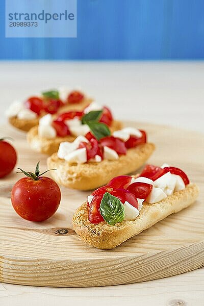 Italian crostini with mozzarella  cherry tomatoes and basil over a chopping board and blue background