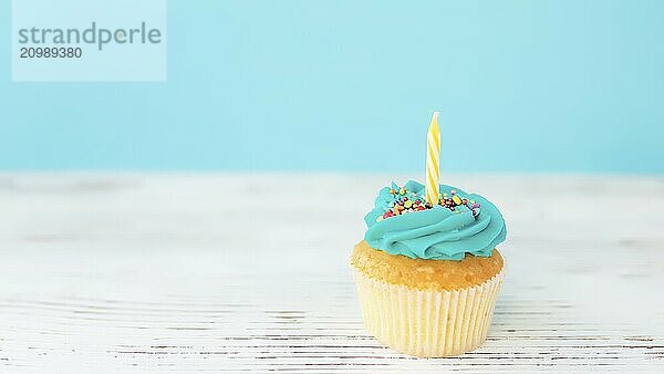 Birthday greetings concept. Yellow candle on a muffin or cupcake. Blue background. Wooden table