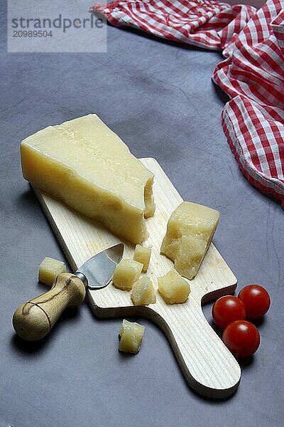 A piece of Parmesan cheese and chopped pieces of cheese on a wooden board