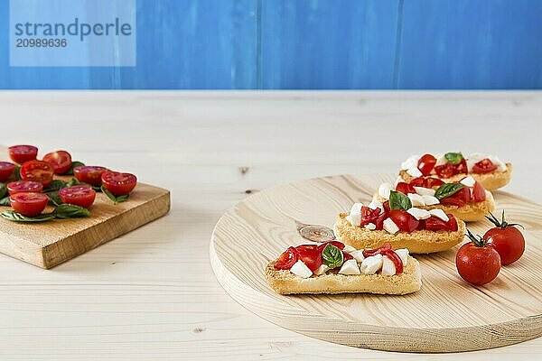 Italian crostini with mozzarella  cherry tomatoes and basil on a chopping board and blue background