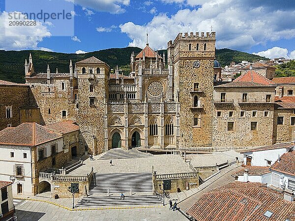 Aerial view of the facade of a monastery with red roofs and wide stairs under a blue sky in Spain. Historical architecture is presented  aerial view  pilgrimage church and monastery  Real Monasterio de Nuestra Señora de Guadalupe  Guadalupe  Cáceres province  Caceres  Extremadura  Spain  Europe