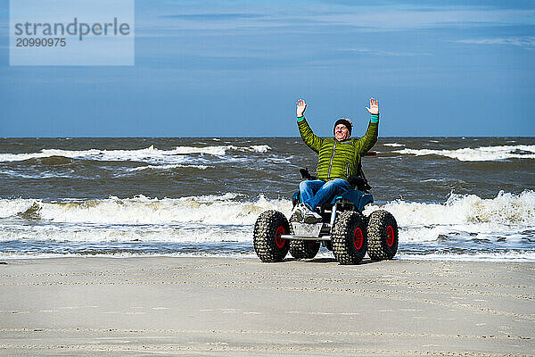 Man in beach wheelchair  raises arms in joy  Sankt-Peter-Ording  Schleswig-Hostein  Germany  Europe