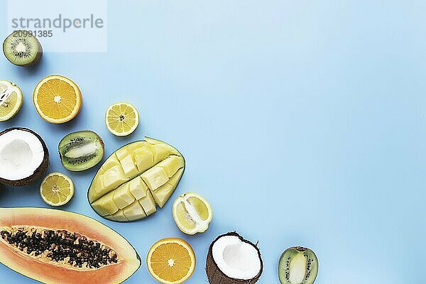 Different fresh tropical cut fruits on a blue background. Papaya  orange  banana  coconut  mango  kiwi and lemon top view flat lay with copy space for some advertisement text