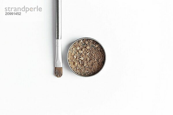 Light brown face shadow in container and eye shadow or make-up brush. Makeup concept flat lay on white background