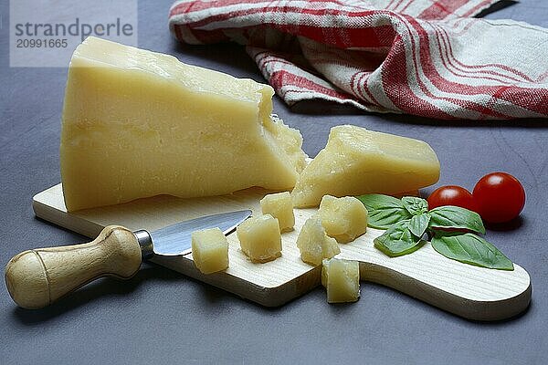 A piece of Parmesan cheese and chopped pieces of cheese on a wooden board