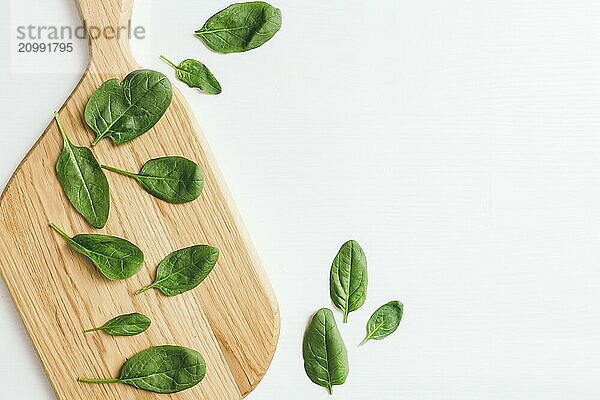 Wooden cutting board with fresh green salad leaves of spinach on white background. Healthy vegetarian eating concept.