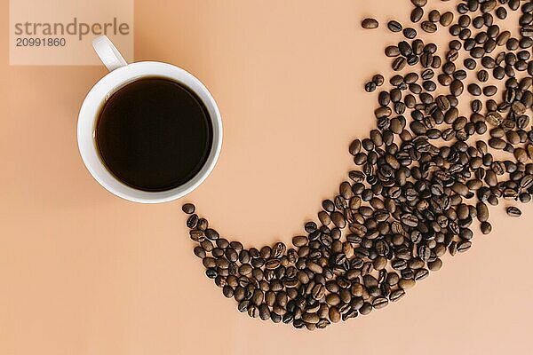 Beige flat lay background with white ceramic cup of coffee  roasted coffee beans steam shape from hot coffee. Idea and composition with coffee beans shape abstraction.