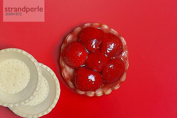 Topped strawberry tartlet and empty tartlet bases on a red background