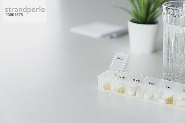 Closeup of medical pill box with doses of tablets for daily take a medicine with white  yellow drugs and capsules used for treatment  cure the disease. Glass cup of water on table  gray background