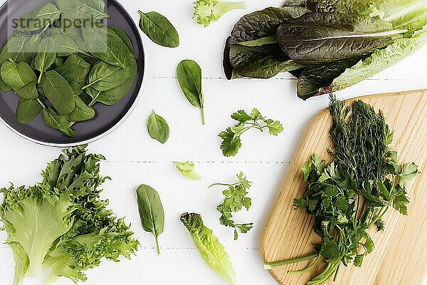 Flat lay with cutting board and bowl of fresh green salad leaves of spinach and lettuce  romaine and parsley  basil on white background. Healthy vegetarian eating concept.