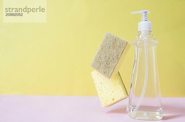 Flat lay with soap dropper  dishwashing liquid  dish soap  washcloth on pastel pink and yellow background.