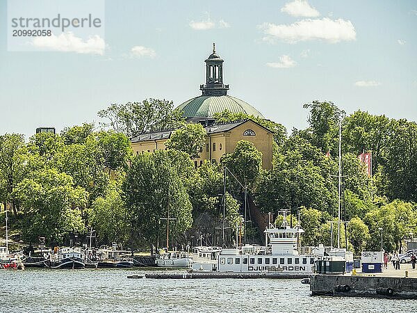 Church with green roof surrounded by trees  in the foreground boats on the water  stockholm  baltic sea  sweden  scandinavia