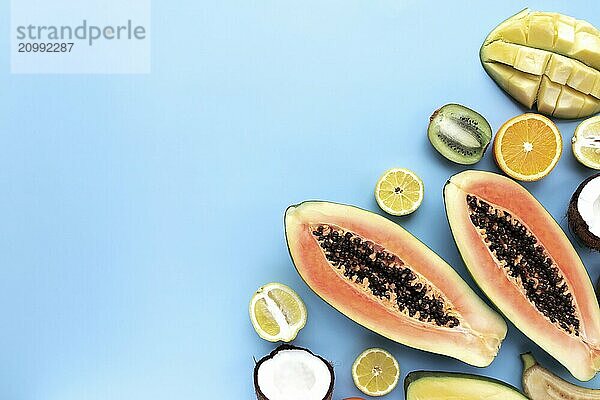 Different fresh tropical cut fruits on a blue background. Papaya  orange  banana  coconut  mango  kiwi and lemon top view flat lay with copy space for some advertisement text