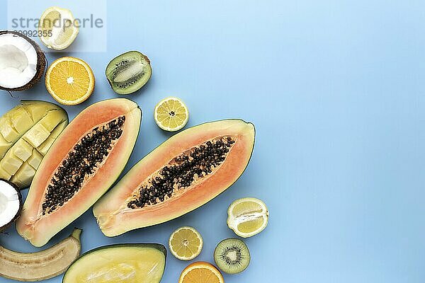 Different fresh tropical cut fruits on a blue background. Papaya  orange  banana  coconut  mango  kiwi and lemon top view flat lay with copy space for some advertisement text