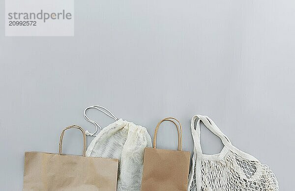 Flat lay with eco white craft paper bags and net bags on gray background with copy space empty advertising area. Packaging template mock up. Delivery service  reusable  recyclable resources concept