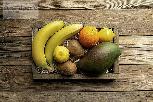 Fresh tropical fruits in a wooden delivery box on a wooden background. Orange  banana  mango  kiwi and lemon top view flat lay with copy space for some advertisement text