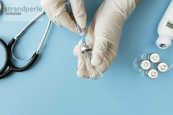 Medicine treatment  vaccination concept. Doctor hands holding bottle with vaccine and injection syringe  electronical thermometer  stethoscope and vaccine vial on blue background.