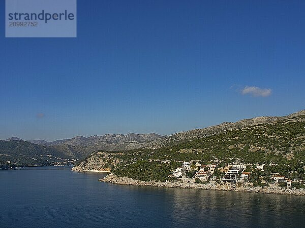 View over the blue sea to a coastal landscape with houses and vegetation on steep cliffs under a blue sky  Dubrovnik  Mediterranean Sea  Croatia  Europe