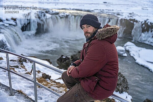 Portrait of a man hiker at frozen Godafoss waterfall at sunset in winter  Iceland  Europe