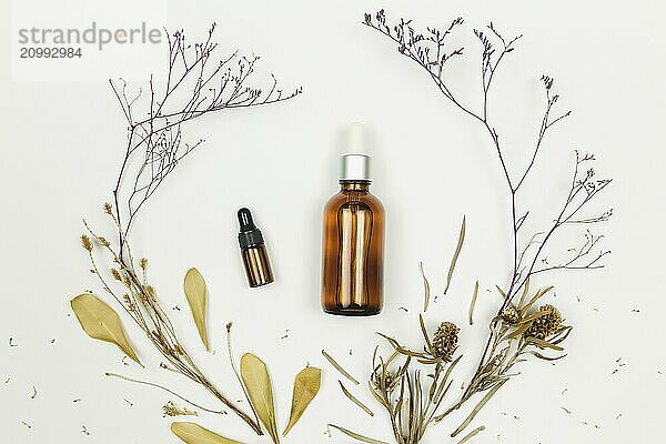 Bottles of cosmetic oil with dried herbs on white background.