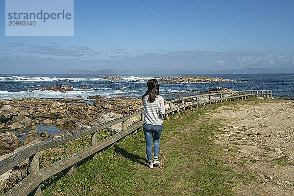 Woman walking on the coast of Galiza in the north of Spain with atlantic ocean and Cies Islands on the background