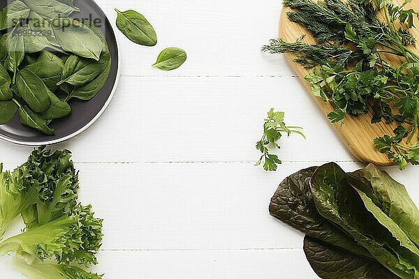 Flat lay with cutting board and bowl of fresh green salad leaves of spinach and lettuce  romaine and parsley  basil on white background. Healthy vegetarian eating concept.