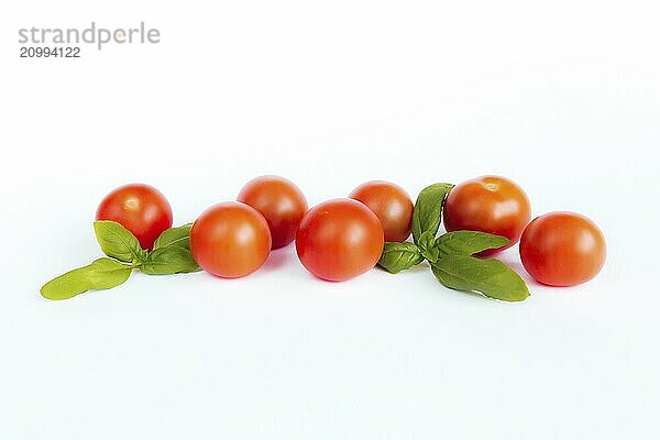 Red cherry tomatoes with green basil on a white background.