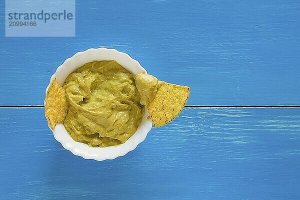 Nachos chips dipping in salsa guacamole over a blue background seen from above