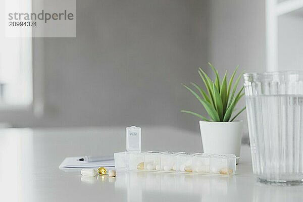 Closeup of medical pill box with doses of tablets for daily take a medicine with white  yellow drugs and capsules used for treatment  cure the disease. Glass cup of water on table  gray background