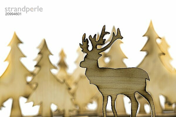 Stag figure sawn out of wood with dark edges and wooden fir trees cut out on white