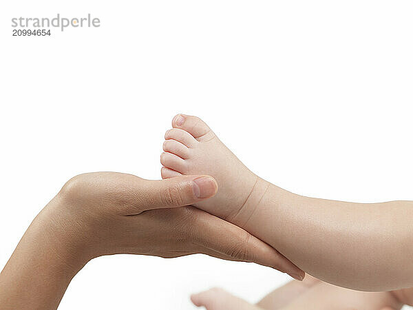 Mother holding her three month old baby sons foot in her hands. Isolated on white background with a clipping path