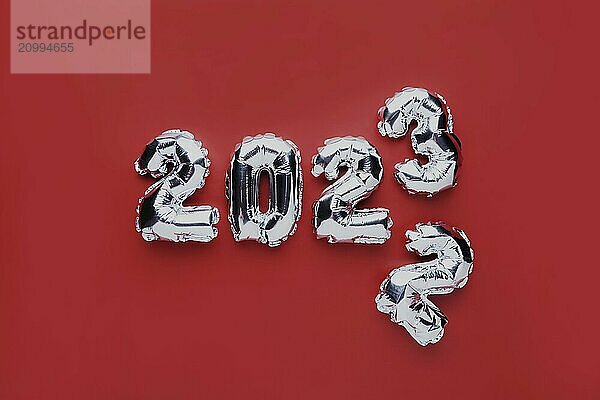 Christmas or New Year background. Red color flat lay with silver shiny 2023 balloon numbers in the center. Simple minimalistic greeting card